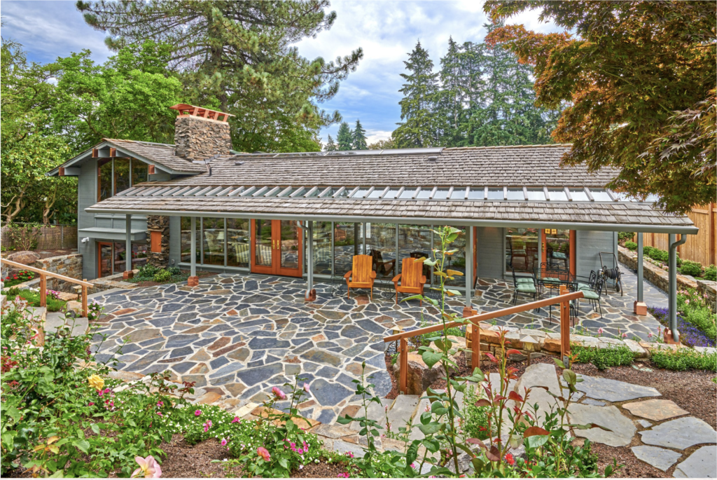 A newly constructed craftsman-style detached accessory dwelling unit with wood beams, a glass awning, and a stone paver courtyard