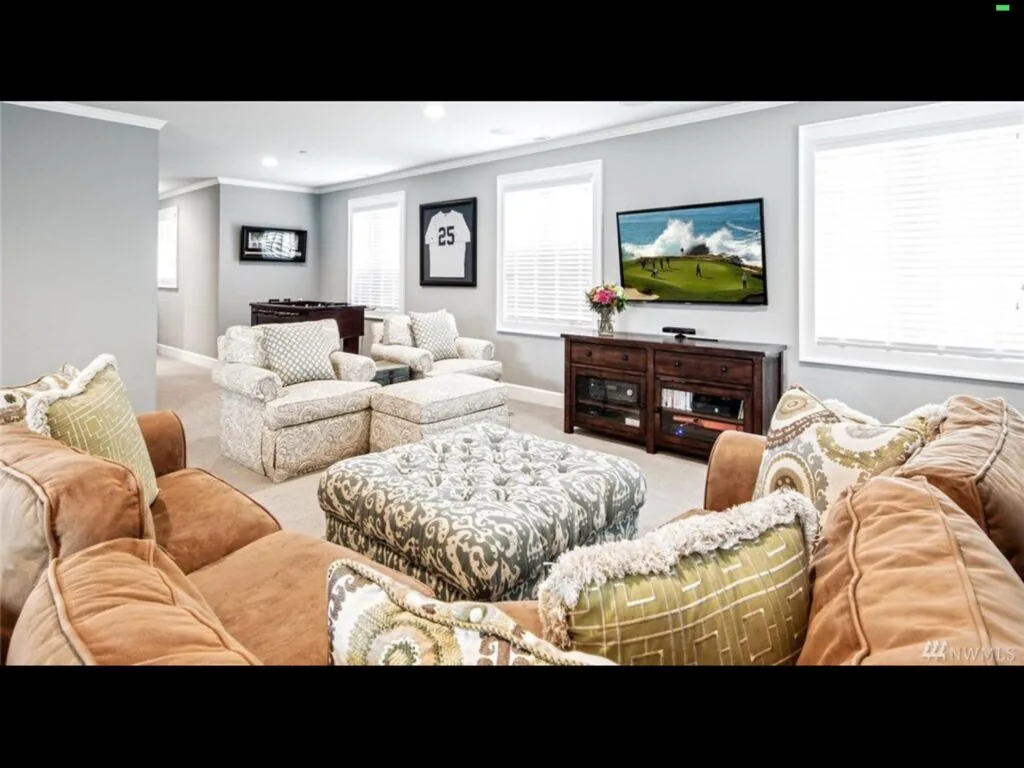 A cozy living room featuring neutral sofas, patterned pillows, a wood media console with a TV, and large windows.💡 Why this works