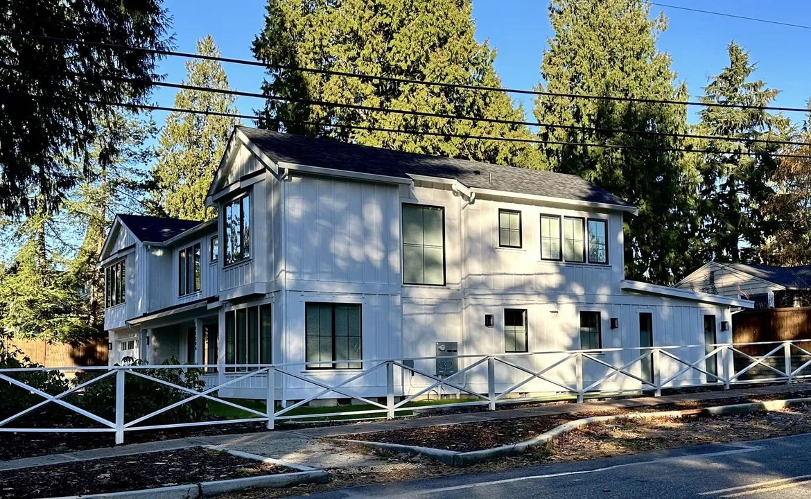 Newly built modern white board-and-batten two-story custom home framed by evergreen trees in the Seattle area, designed by Piper Cole Architects.