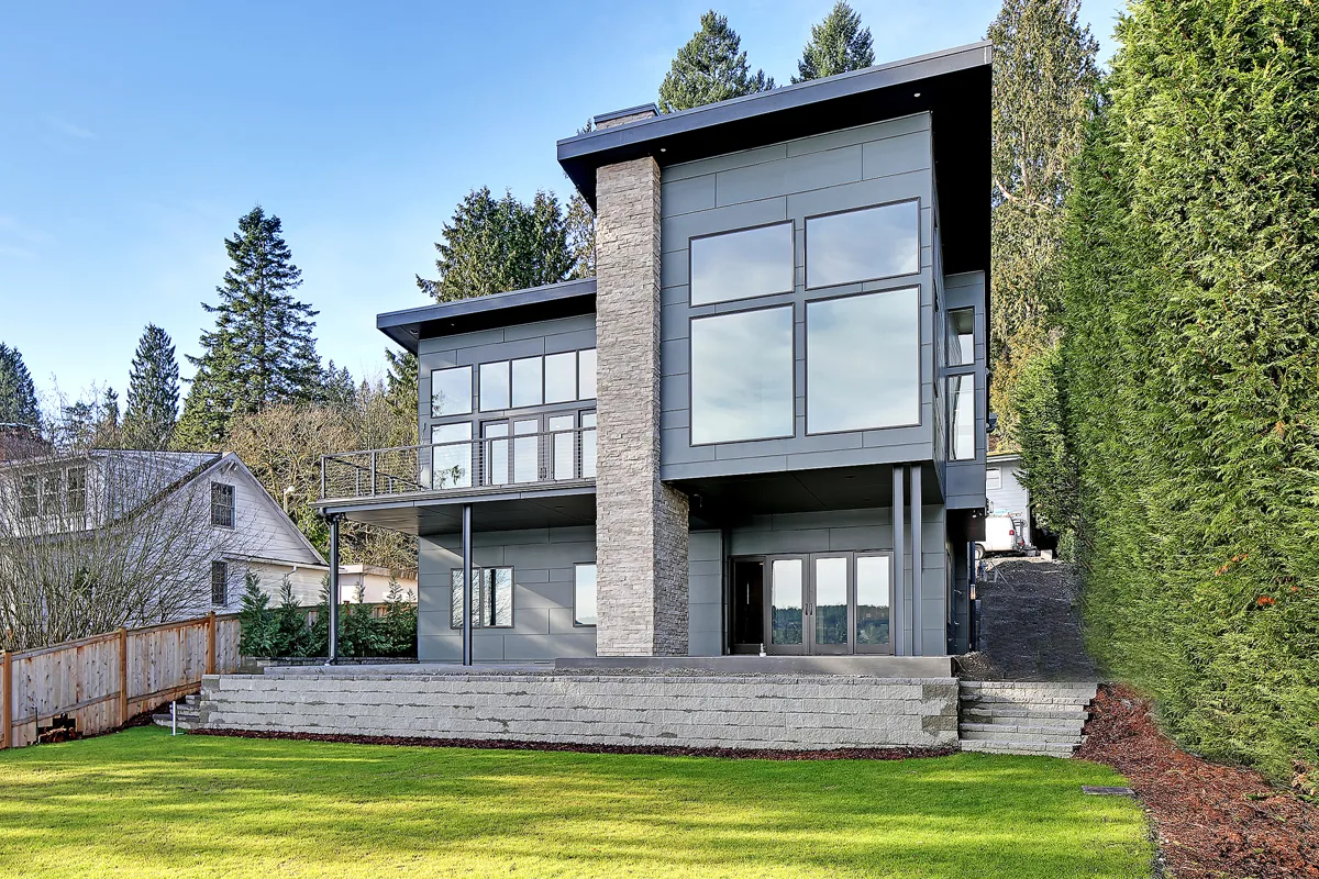 Rear exterior of a modern two-story home with large windows and mixed stone-and-siding cladding in the Seattle area, a second-story addition designed by Piper Cole Architects.