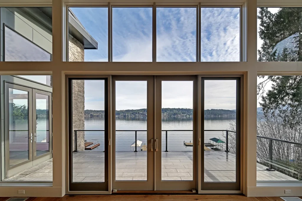 Floor-to-ceiling windows and glass doors flooding a Seattle-area home with daylight and framing a lake view, a biophilic design by Piper Cole Architects.