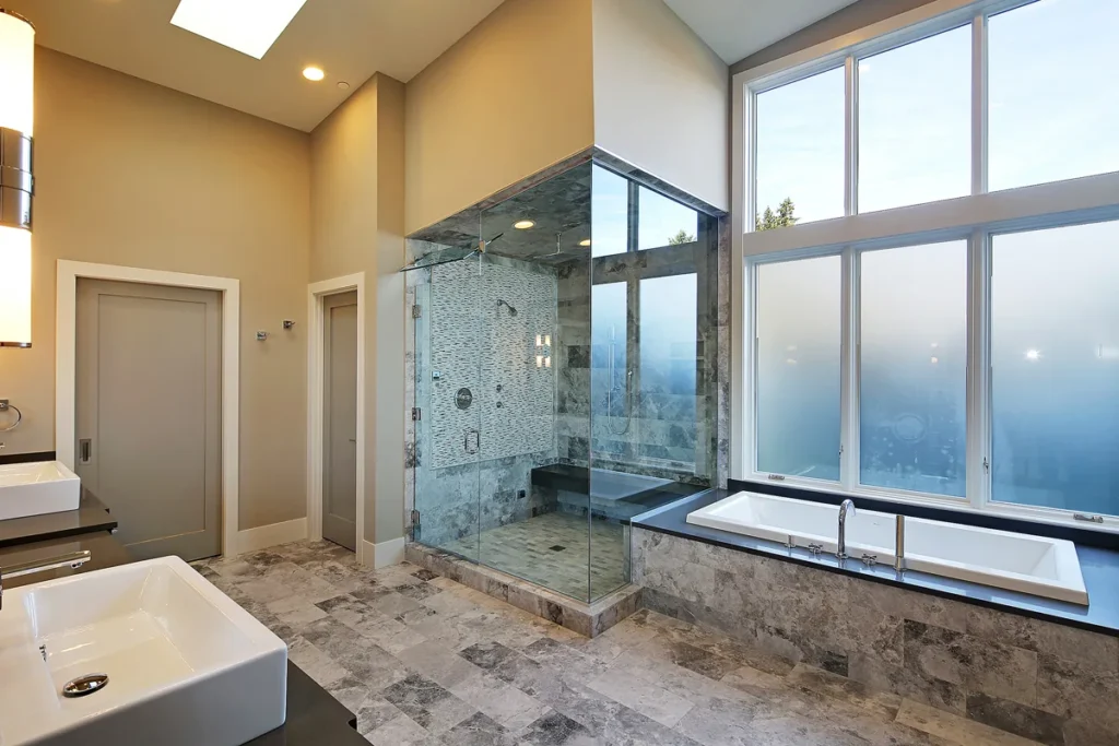 Primary suite bathroom with a glass walk-in shower, soaking tub, and floor-to-ceiling windows in a Seattle Eastside home by Piper Cole Architects.