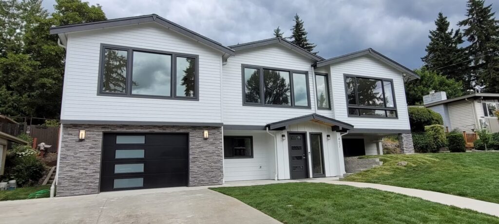 Remodeled split level house with white siding, stone base, black windows and modern garage door