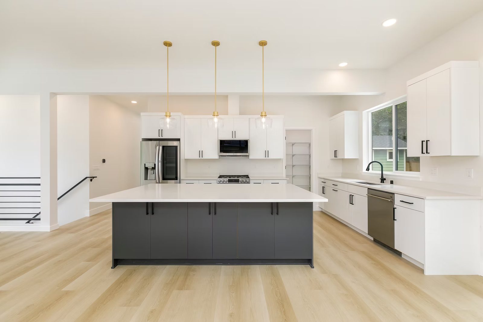 A white kitchen with a charcoal island, brass pendants and a light oak plank floor