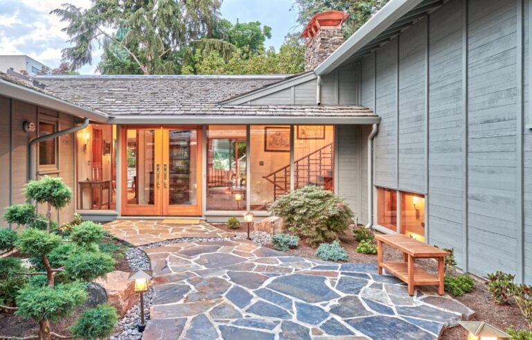 Flagstone entry courtyard with pruned pines leading to wood French doors and glass entry hall