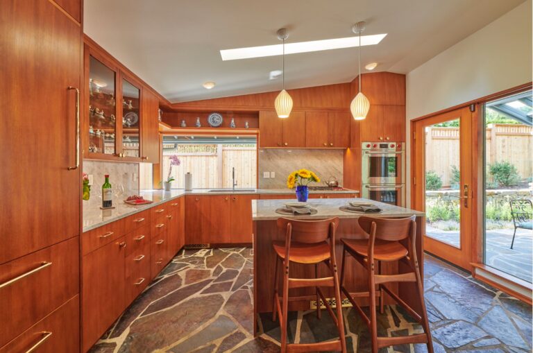 Kitchen with cherry cabinets, marble counters, island seating, skylight and slate floor opening to patio