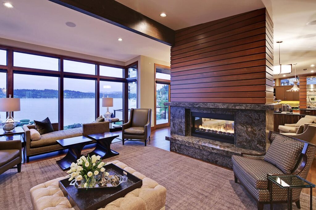 Living room with wood-clad see-through fireplace and floor-to-ceiling windows facing the lake