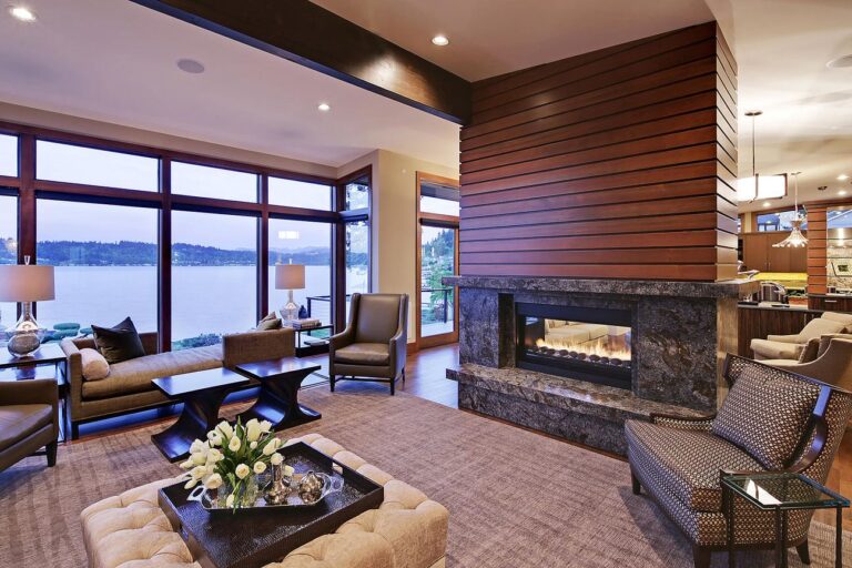 Living room with wood-clad see-through fireplace and floor-to-ceiling windows facing the lake