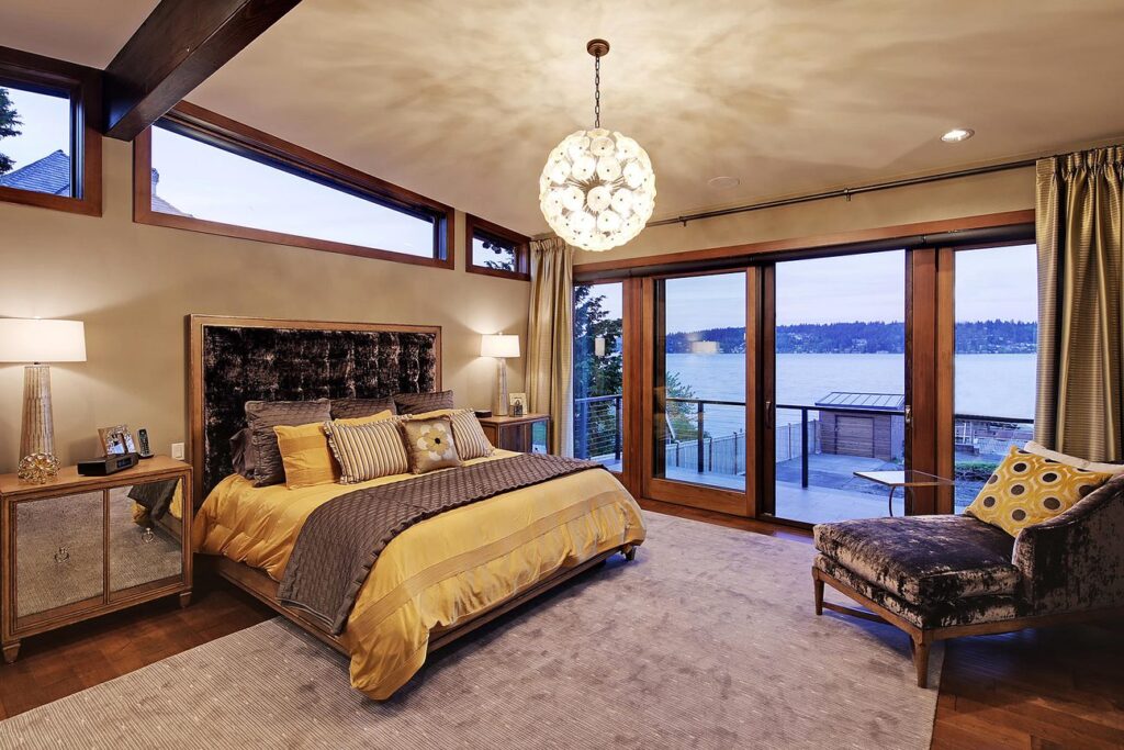 Primary bedroom with upholstered headboard, globe pendant and sliding doors to a lake view deck