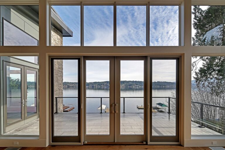 Tall window wall and French doors opening to a deck with cable rail and lake view